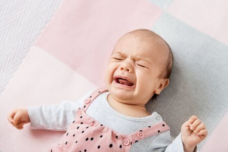 crying baby girl lying on knitted blanketの写真素材