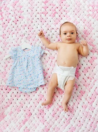 Baby girl in diaper lying with dress on blanketの写真素材