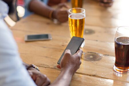 man with smartphone drinking beer at bar or pubの写真素材