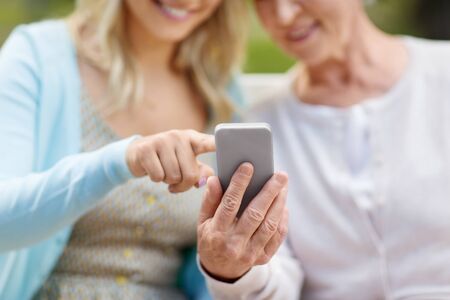 daughter and senior mother with smartphone at parkの写真素材