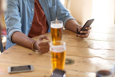 People and technology concept - Man with smartphone drinking beer and reading message at bar or pubの写真素材