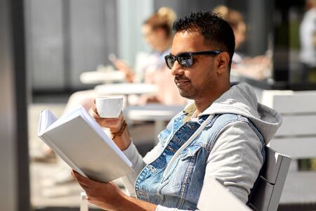 man reading book and drinking coffee at city cafe