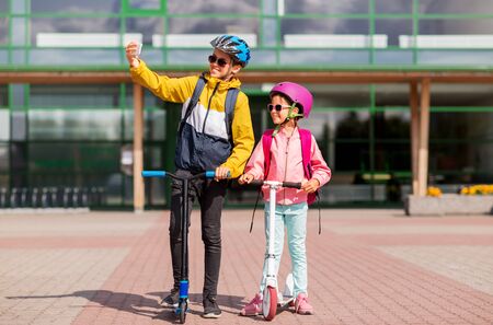 happy school kids with scooters taking selfieの写真素材