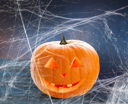 holidays, halloween and decoration concept - pumpkin or jack o lantern on table and spiderweb over starry night sky backgroundの写真素材