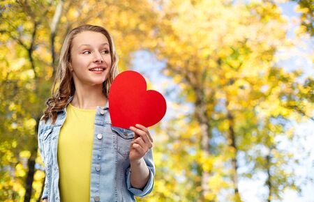 smiling teenage girl with red heart in autumn parkの写真素材