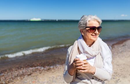 senior woman drinking takeaway coffee on beachの写真素材