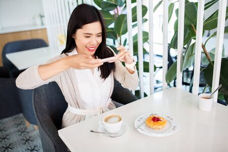 technology, leisure and people concept - happy asian woman with smartphone photographing her coffee...
