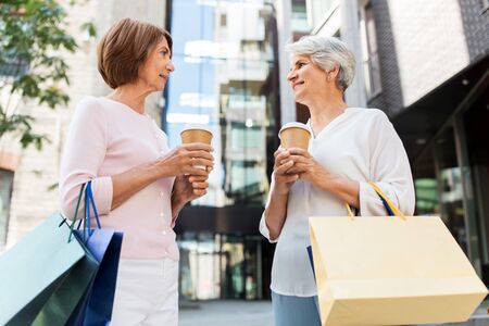 senior women with shopping bags and coffee in cityの写真素材