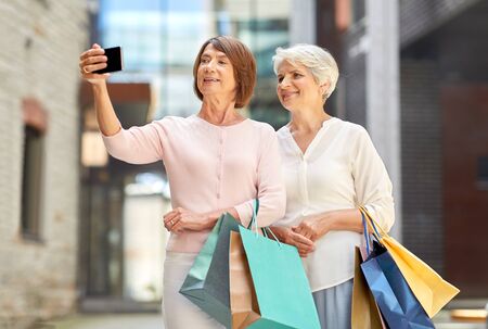 old women with shopping bags taking selfie in cityの写真素材