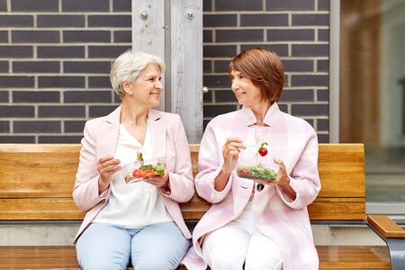 senior women eating takeaway food on city streetの写真素材