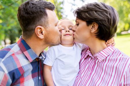 mother and father kissing their little son at parkの写真素材