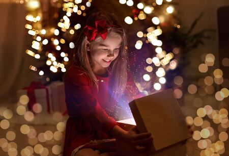 smiling girl opening christmas gift at nightの写真素材