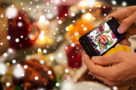 Close up of male hands photographing roast turkey by smartphone at christmas dinner over snowの写真素材