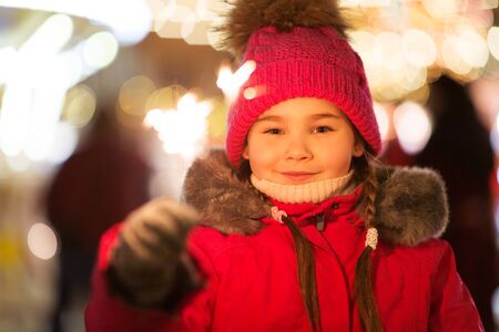 Happy little girl with sparkler at christmas market in winter eveningの写真素材