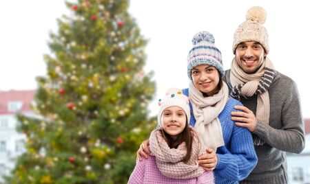 Happy mother, father and little daughter in knitted hats and scarves over christmas tree in old town of tallinn cityの写真素材