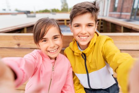 children sitting on street bench and taking selfieの写真素材