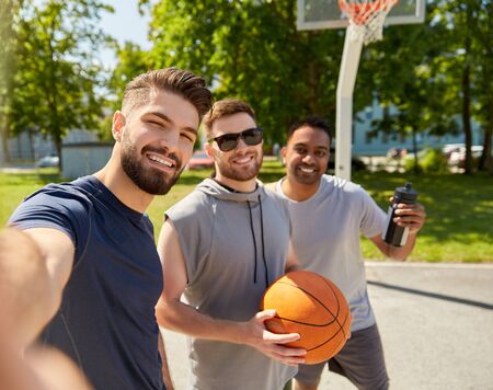 sport, leisure games and male friendship concept - group of happy men or friends taking selfie on outdoor basketball playgroundの写真素材