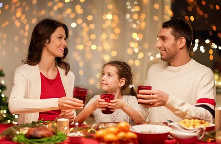 holidays, family and celebration concept - happy mother, father and little daughter with drinks toasting at home christmas dinnerの写真素材