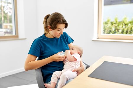 family, babyhood and people concept - mother feeding baby daughter with milk formula from bottle
