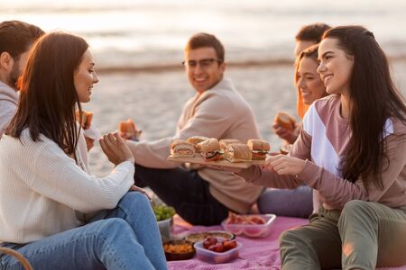 happy friends eating sandwiches at picnic on beach