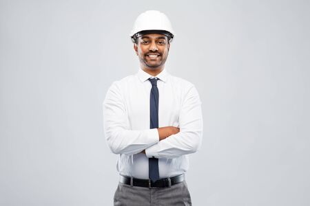 smiling indian male architect in helmet over greyの写真素材