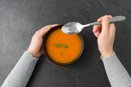 hands with bowl of pumpkin cream soup on tableの写真素材
