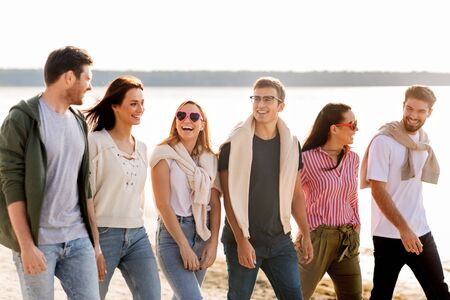 happy friends walking along summer beach