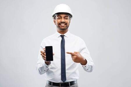 indian male architect in helmet showing smartphone
