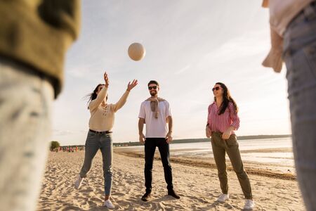 volleyball, leisure games and people concept - happy friends playing with ball on beach in summerの写真素材
