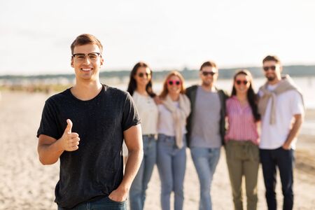 friendship, leisure and people concept - happy man with group of friends on beach in summer showing thumbs upの写真素材