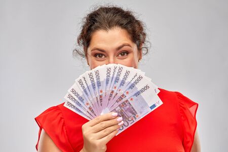 people and finances concept - happy woman in red dress hiding her face behind euro money banknotes...