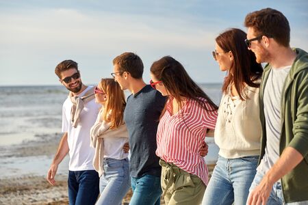 happy friends walking along summer beach
