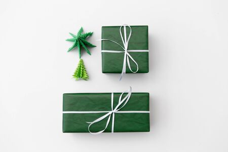winter holidays, new year and celebration concept - gift boxes wrapped into green paper and origami christmas trees on white backgroundの写真素材
