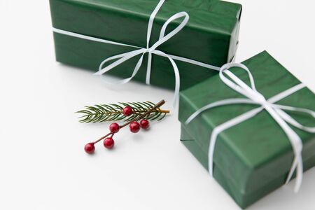 winter holidays, new year and christmas concept - gift boxes wrapped into green paper and fir tree branch with red berries on white backgroundの写真素材