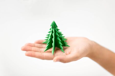 winter holidays, new year and craft concept - hand holding green paper origami christmas treeの写真素材