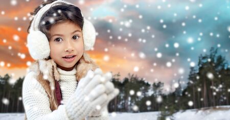 happy little girl in earmuffs over winter forestの写真素材