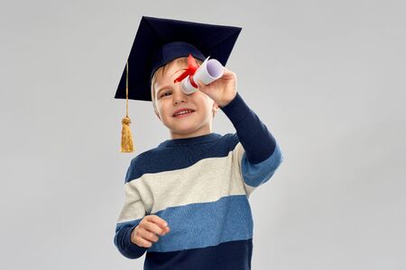 little boy in mortarboard looking through diplomaの写真素材