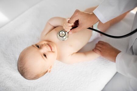 medicine, healthcare and pediatrics concept - close up of female doctor with stethoscope listening to baby girl's patient heartbeat or breath at clinic or hospitalの写真素材
