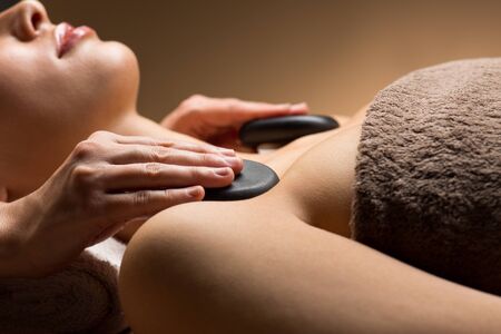 wellness, beauty and relaxation concept - close up of young woman having hot stone massage at spaの写真素材