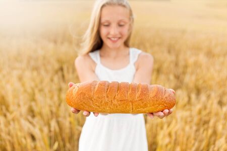 prosperity, harvesting and thanksgiving concept - smiling young girl holding loaf of white bread on...