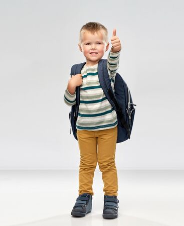 preschool education and childhood concept - portrait of smiling little boy with school backpack over grey backgroundの写真素材