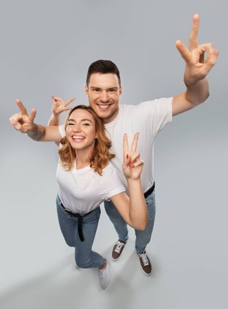 gesture and people concept - portrait of happy couple in white t-shirts showing peace over grey backgroundの写真素材