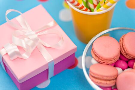 birthday party, celebration and decoration concept - gift box, pink macarons, paper straws and...
