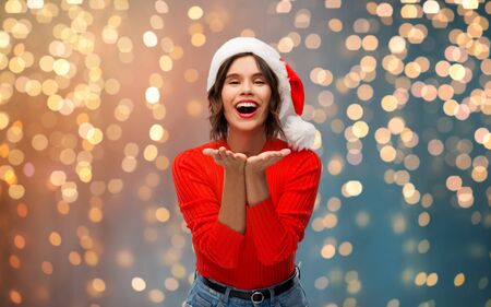 christmas, holidays and people concept - happy smiling young woman in santa helper hat sending air kiss over grey backgroundの写真素材