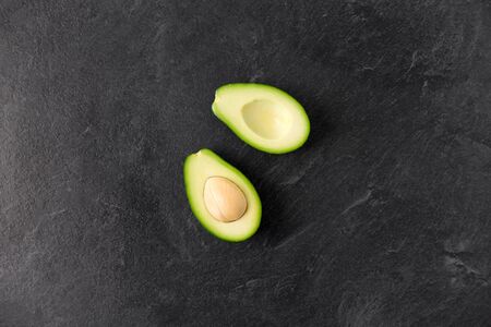 food, eating and vegetable concept - close up of cut avocado with bone on slate stone background