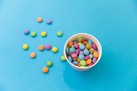 food, confectionery and sweets concept - candy drops in paper cup on blue backgroundの写真素材