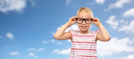 smiling little girl in glasses over sky backgroundの写真素材