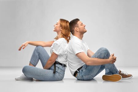 relationships, style and people concept - happy couple in white t-shirts sitting on floor over grey backgroundの写真素材