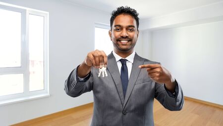 real estate business and people concept - indian man realtor with keys over empty new apartment room backgroundの写真素材