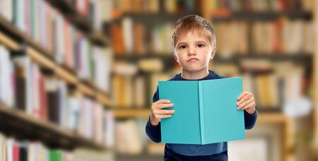 displeased little boy reading book over libraryの写真素材